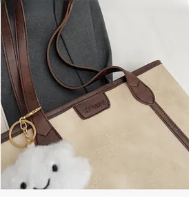 Detail of beige tote bag featuring brown leather trim and a white plush cloud charm