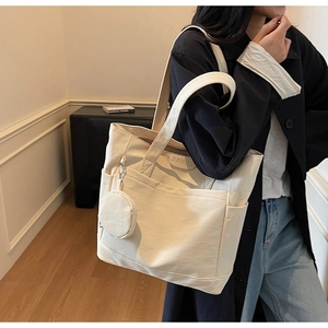 Detail of minimalist cream tote bag showing side pocket and round coin purse pendant