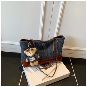 Detailed close-up of denim tote bag with leather trim and bear plush keychain charm