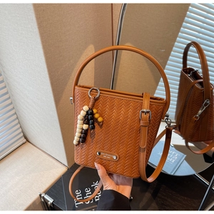 Detailed view of brown woven bucket bag featuring wooden bead charm and sleek handle