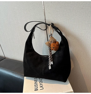 Close-up of black suede hobo bag with silver zipper and brown plush bear charm