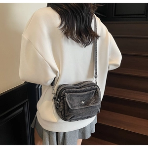 Detail view of dark grey denim crossbody bag with adjustable strap and silver metal snap button
