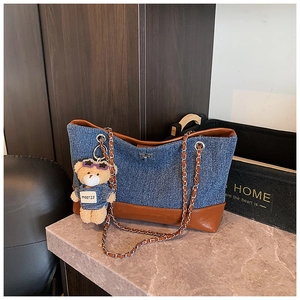 Detail of denim tote bag with brown leather trim and a cute teddy bear charm