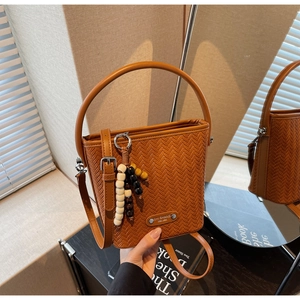 Brown woven bucket bag featuring circular top handle and colorful beaded pendant detail