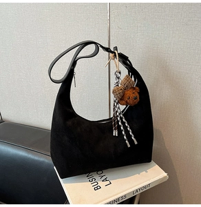 Detail of black suede hobo bag with a zipper closure and a cute brown bear charm
