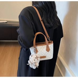 Close-up of checkerboard tote bag with brown leather handles and a plush rabbit charm