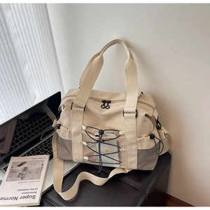 Détail d'un sac de voyage beige avec poignées tissées posé sur une chaise en cuir noir