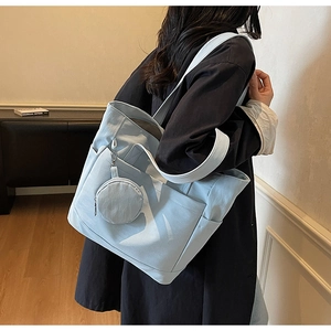 Detail of light blue tote bag with a matching coin purse charm shown on a shoulder