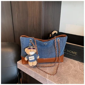 Detail of denim and brown leather patchwork tote bag with metal chain strap and bear charm