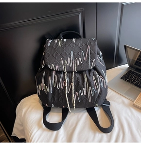 Detail of a black quilted backpack with colorful wave embroidery on a white bed surface