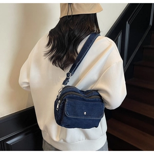 Detail of dark blue denim crossbody bag with silver hardware and adjustable strap