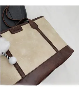 Close-up of cream and brown tote bag featuring a leather logo tag and plush ball charm