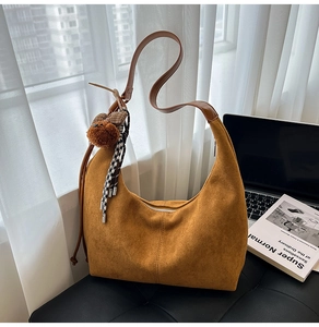 Detail of caramel suede hobo bag with plush bear charm and checkered tassel on a desk