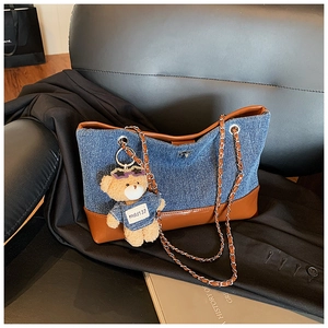 Detail of denim and brown leather tote bag with metal chain strap and cute bear charm