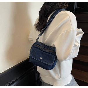 Detail of blue denim crossbody bag with metal snap button worn by a model in a casual setting