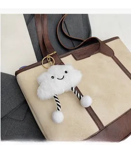 Close-up of white plush cloud charm with smiley embroidery on a beige tote bag
