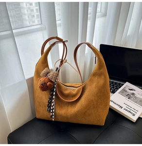 Close-up of brown suede hobo bag with teddy bear pendant and premium stitching details