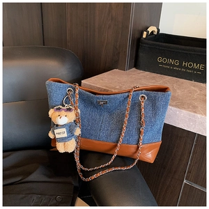 Detail of denim tote bag with leather trim and cute bear charm on a metal chain strap