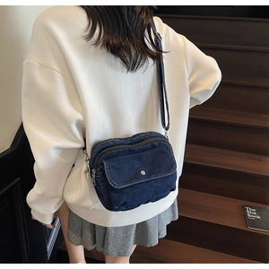 Detail of dark blue denim crossbody bag with adjustable strap and silver metal buckle