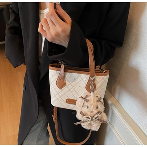 Detail of checkered tote bag featuring brown leather trim and a cute plush rabbit charm