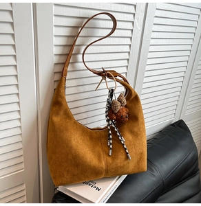 Detail of tan suede hobo bag with a plush bear charm on a vintage leather sofa
