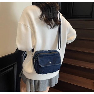 Detail view of dark blue denim crossbody bag worn over shoulder in casual style