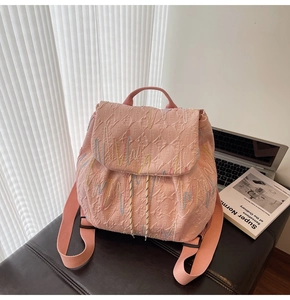 Pink backpack with textured 3D pattern and colorful wavy embroidery on a dark leather bench