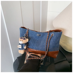 Detail of denim tote bag with leather trim, metal chain strap and cute bear charm pendant