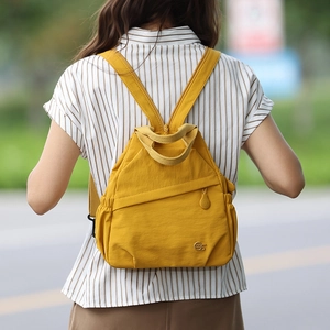 Outdoor close-up of a mustard yellow nylon backpack with premium metal logo detail