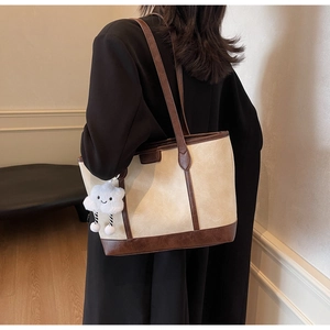 Detail of off-white tote bag with brown leather trim and plush cloud charm accessory