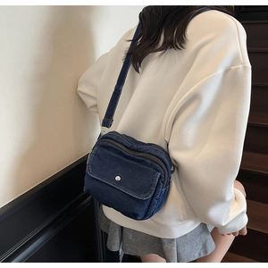 Detail of dark blue denim crossbody bag featuring a front flap and silver metal buckle