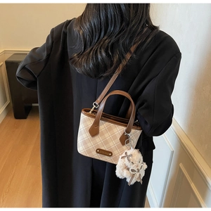 Detail view of checkerboard tote bag with plush bear charm worn on the shoulder