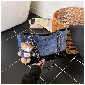 Detail of denim tote bag with shiny leather trim, silver chain, and cute brown bear charm