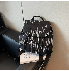 Detail of black quilted backpack with wave embroidery on leather sofa scene