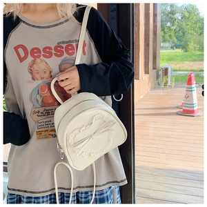 Détail d'un sac à dos blanc crème avec dentelle cœur, grand nœud et fermeture éclair en métal
