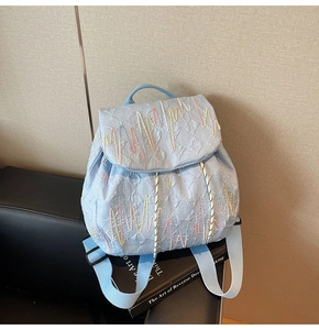Detail view of light blue quilted backpack with letter E embroidery on a leather seat