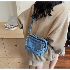 Detail view of the blue denim crossbody bag worn by a model in a casual indoor setting