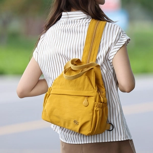 Outdoor shot of mustard yellow nylon backpack showing front zip pocket and straps