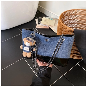 Detail shot of the denim and patent leather tote bag with a plush bear charm and metal chain