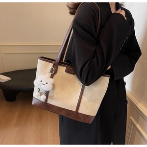 Close-up of cream tote bag with brown trim, logo plaque, and fluffy cloud charm