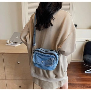 Blue denim crossbody camera bag with dual zip compartments shown on a model's back