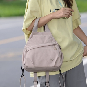Detail of a light pink nylon backpack featuring metal MS logo and sleek front zipper pocket