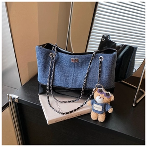 Detail of denim and patent leather tote with silver twist lock and plush bear charm