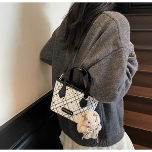 Fashionable checkerboard tote bag with a cute white plush bunny charm on a dark staircase