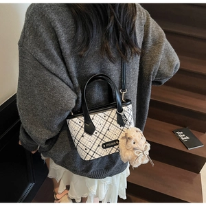 Detail of checkered tote bag with plush rabbit charm and metal logo plaque on textured body
