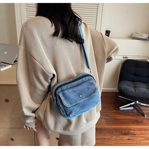 Detailed shot of a blue denim crossbody bag featuring multiple functional zipper pockets