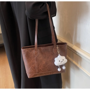 Detail view of brown leather tote bag with white plush cloud charm and embossed logo