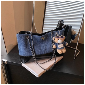Detail of denim tote bag with leather trim, metal chain strap and blue bear charm