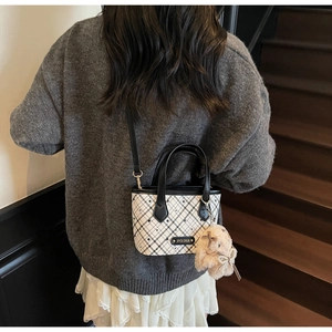 Detail of checkered tote bag with pink rabbit charm shown on a shoulder in a lifestyle setting