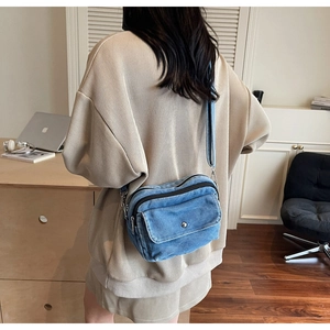 Blue denim crossbody bag featuring a front flap pocket and dual zipper compartments